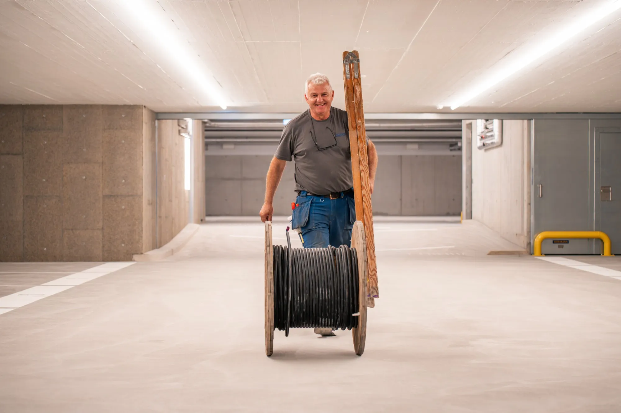 Elektriker von GalaTech zieht eine Kabelrolle durch eine neue Tiefgarage und trägt eine Holzleiter