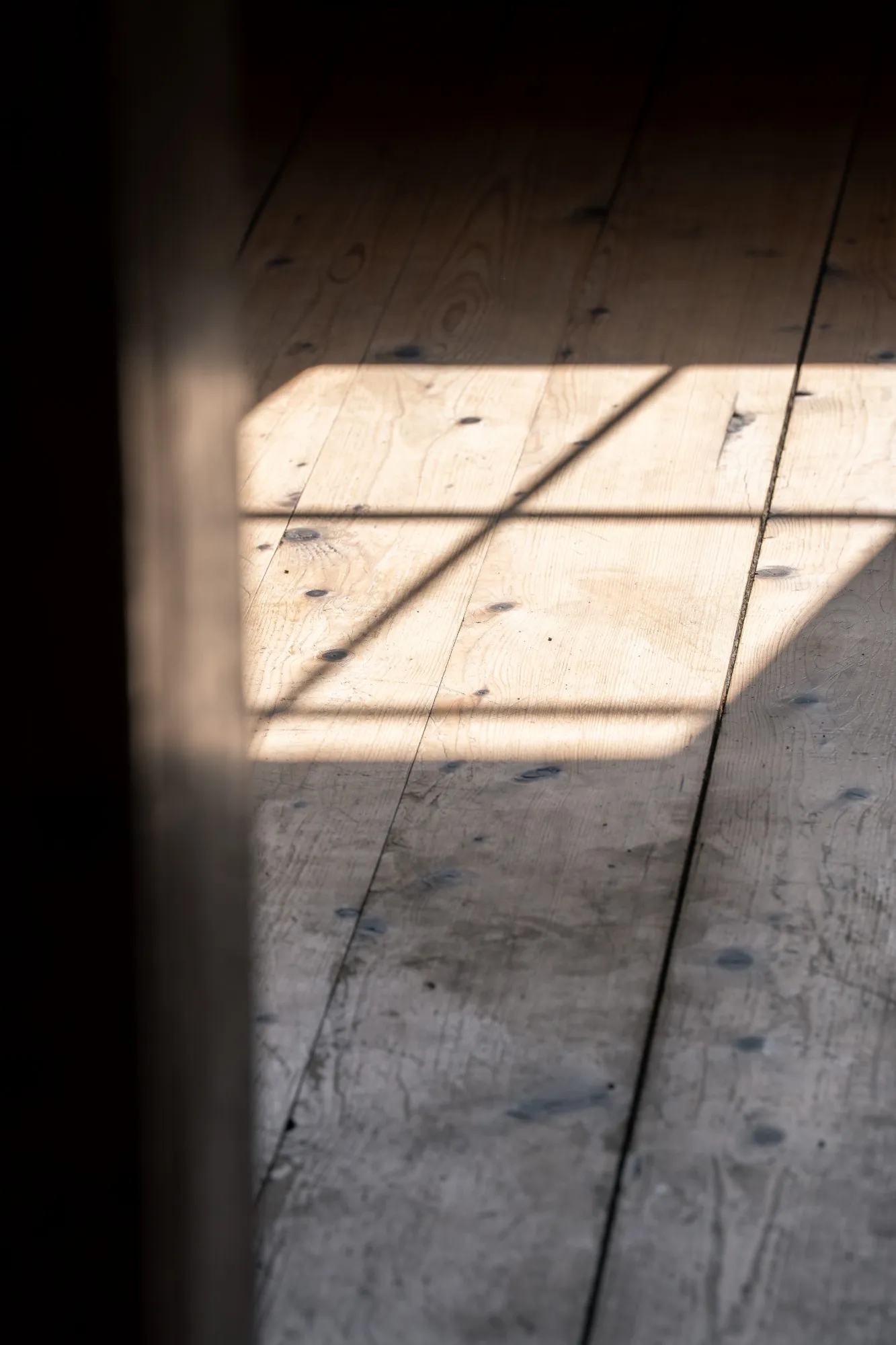 Sonnenlicht mit Fensterkreuz auf einem alten Bohlenboden