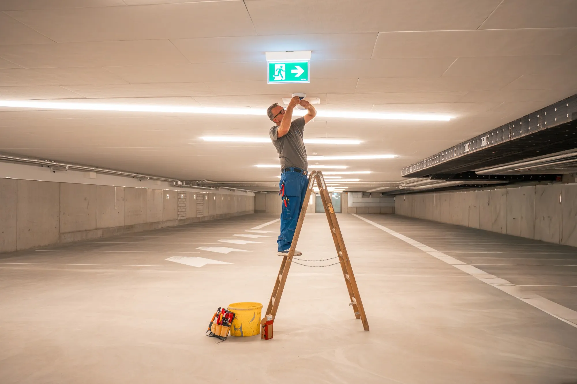 Elektriker von GalaTech montiert auf einer Holzleiter einen Sensor an der Decke einer Tiefgarage