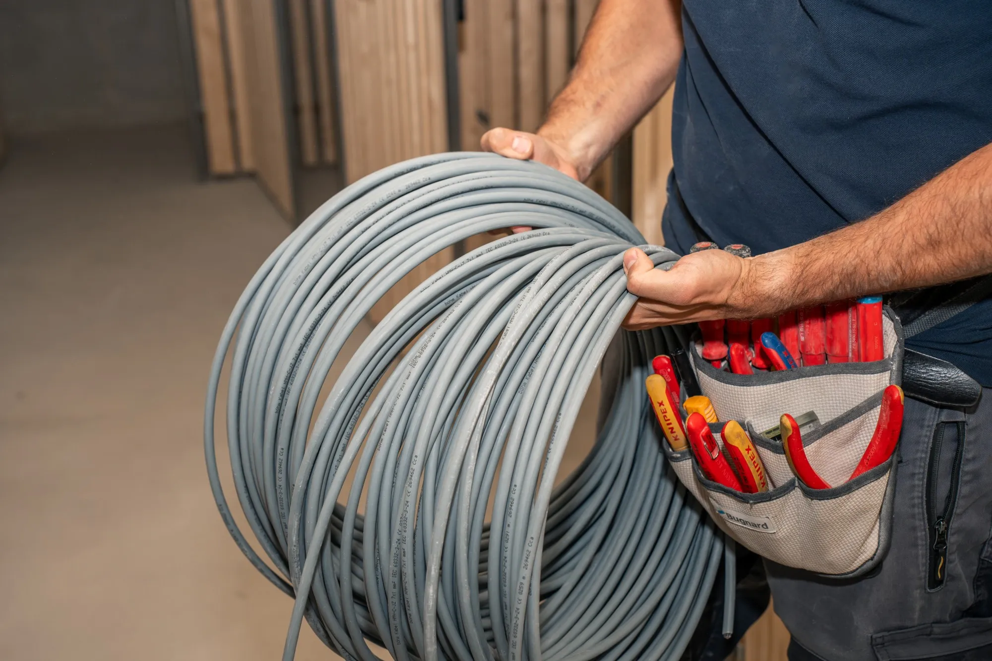 Elektriker trägt einen Kabelring, an der Hüfte eine Werkzeugtasche mit Zangen und Schraubenziehern