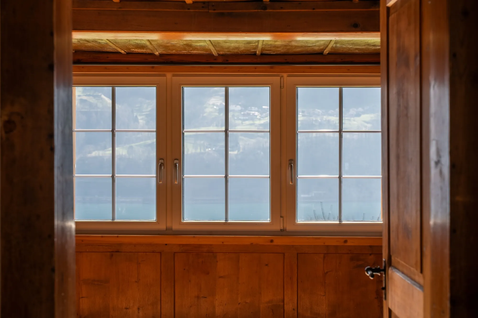 Blick durch eine Tür auf drei Sprossenfenster mit Aussicht auf den See