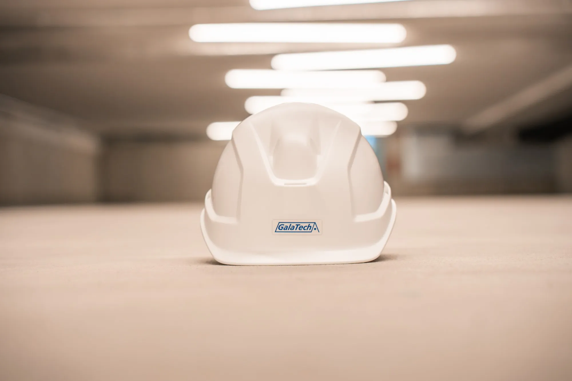 Weisser Bauhelm mit GalaTech-Logo auf dem Boden einer beleuchteten Tiefgarage