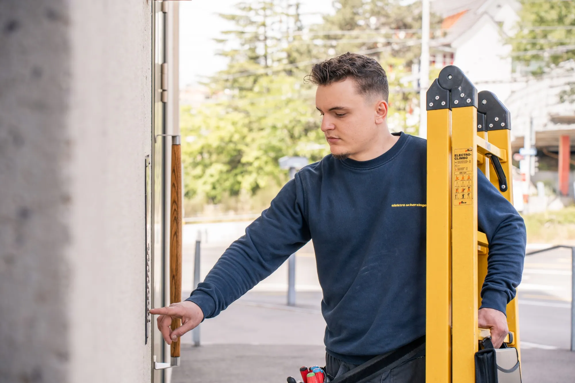 Junger Elektriker von Elektro Scherzinger mit Leiter klingelt an einer Haustür