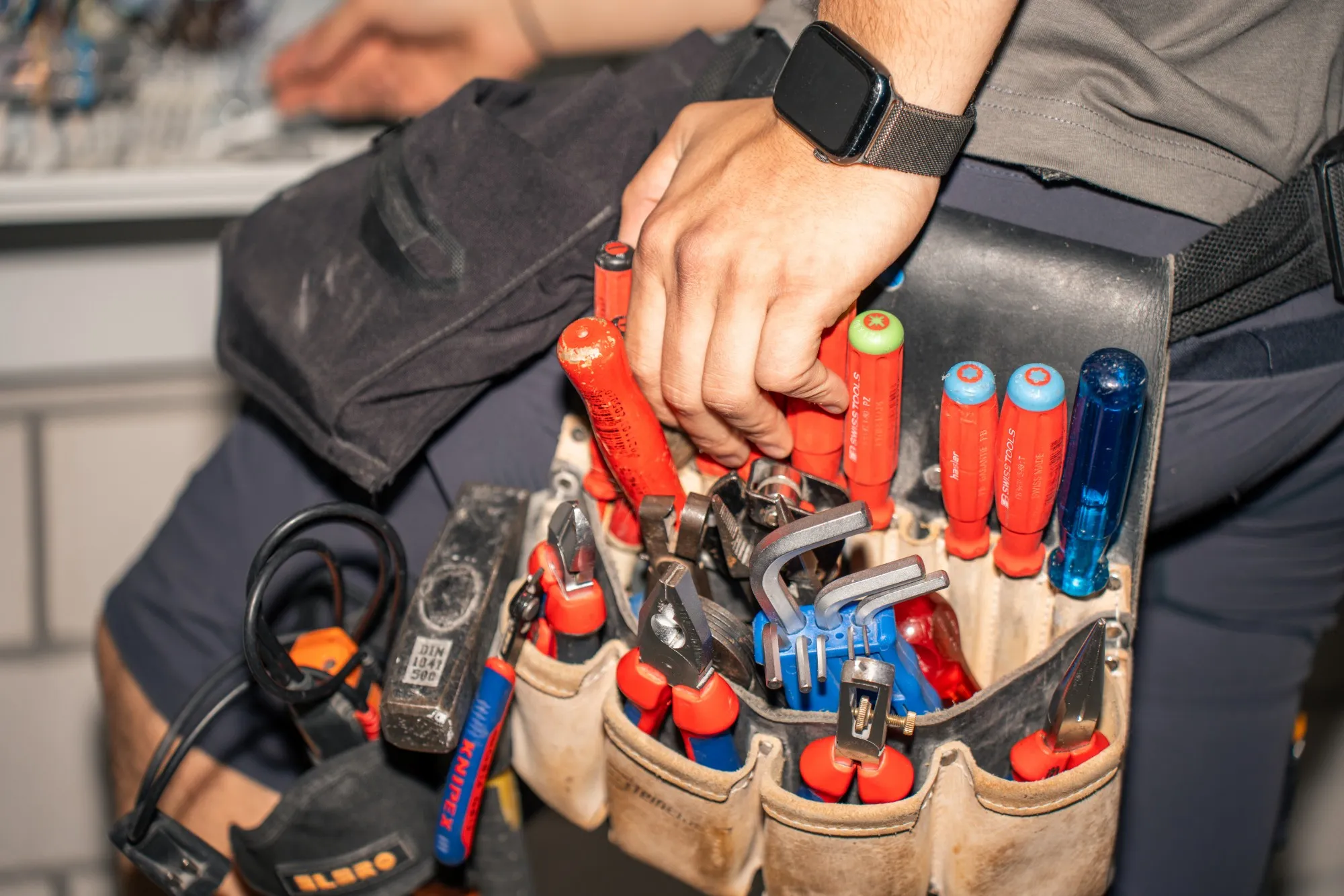 Hand greift in eine Werkzeugtasche voller Schraubenzieher und Zangen