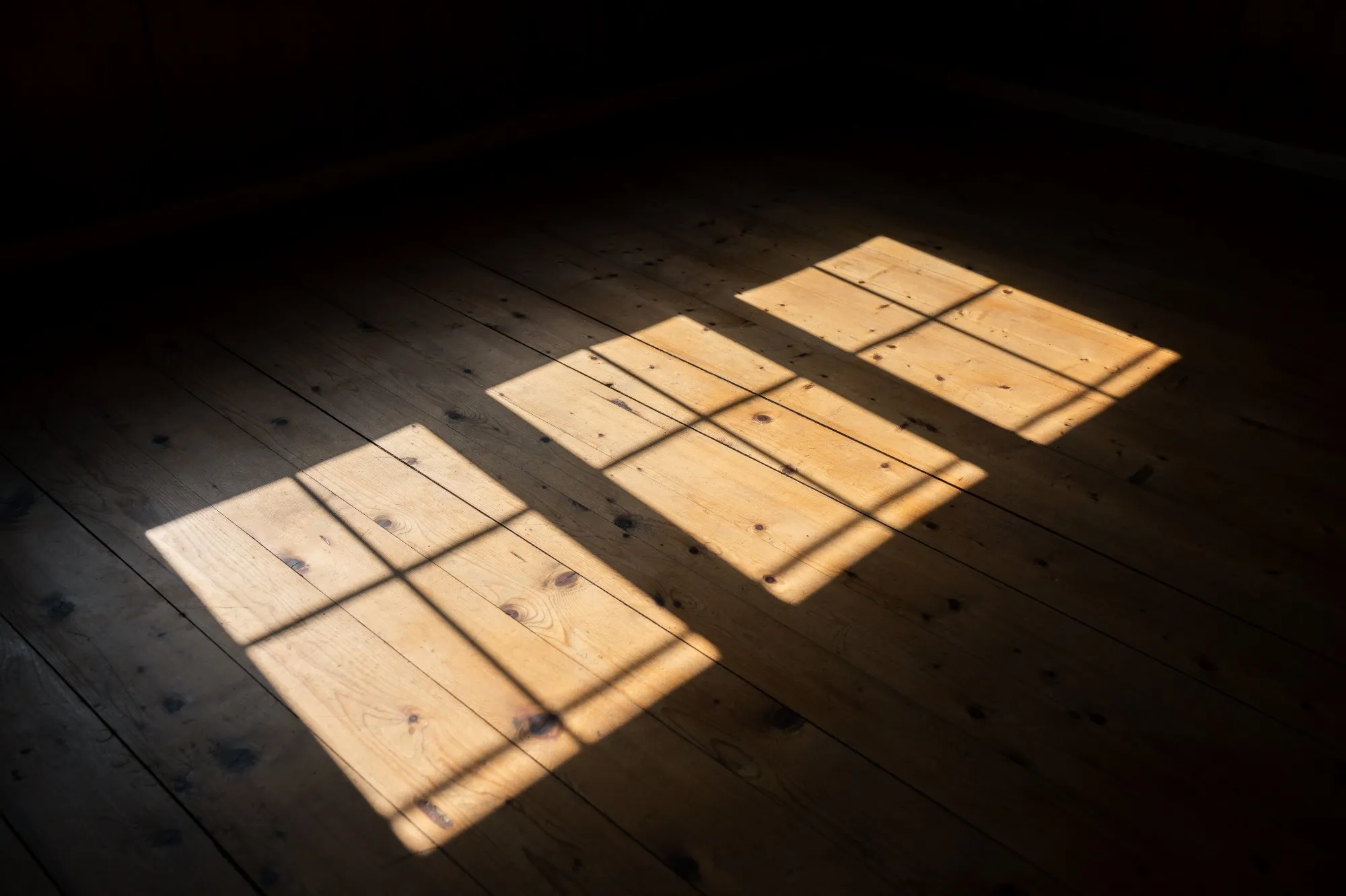 Drei Lichtflecken der Fenster auf einem dunklen Holzboden