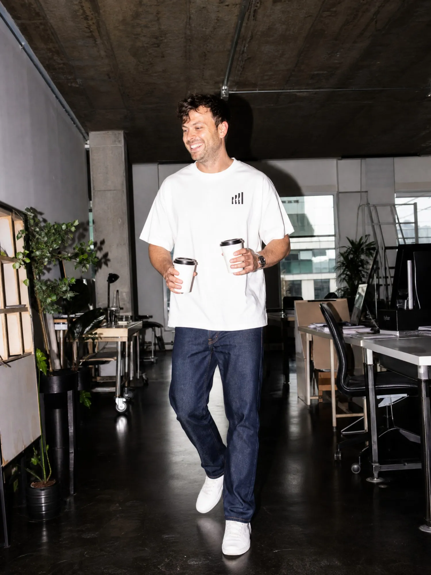 Mäx Känzig im allkind-Shirt, lachend, mit zwei Kaffeebechern in den Händen
